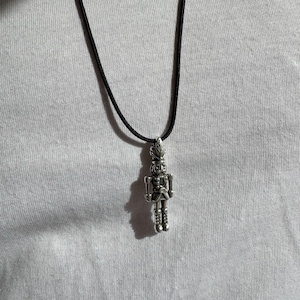 Peut inclure: Un collier avec un pendentif en forme de casse-noisette argenté sur un cordon noir.