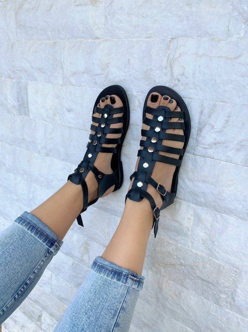 Puede incluir: Sandalias gladiadoras de cuero negro con hebillas y tachuelas plateadas. Las sandalias tienen un dise&ntilde;o enjaulado y se usan en los pies.