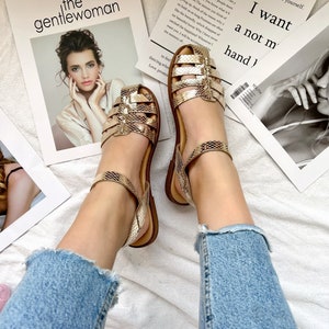 Puede incluir: Un par de sandalias doradas de piel de serpiente con una gruesa correa de tobillo. Las sandalias est&aacute;n sobre una superficie blanca con una revista que presenta el texto "the gentlewoman" y otra revista con el texto "GIVE ME sometimes the same thing we can go to the comfort of others, but failed to convince yourself. I want a not m hand)"