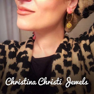 Puede incluir: Pendientes de aro dorados con un dije circular. Los pendientes se llevan con un su&eacute;ter con estampado de leopardo. El texto "Christina Christi Jewels" se muestra en la parte inferior de la imagen. Joyas.