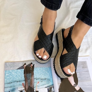 May include: Black platform sandals with a woven design and a jute-wrapped sole. The sandals have a criss-cross strap design and a buckle closure. The platform sole measures approximately 2 inches (5 cm) high.