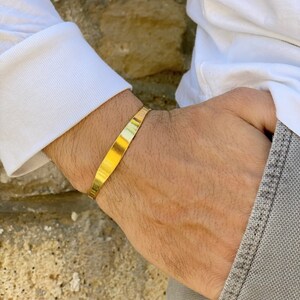 May include: A gold-colored metal cuff bracelet on a person's wrist.