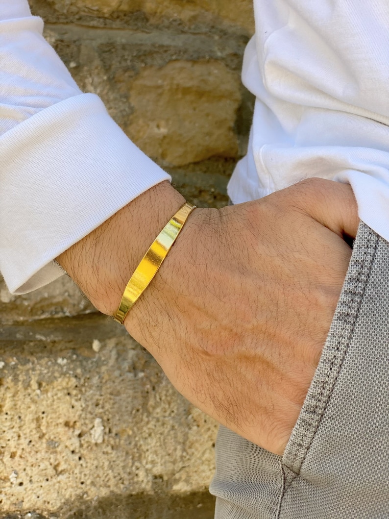 May include: A gold-colored metal cuff bracelet on a person's wrist.