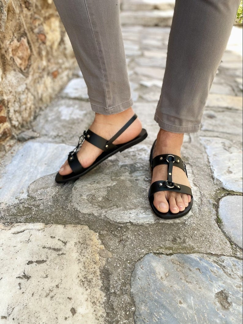 Puede incluir: Sandalias de cuero negro con hebilla y correas. Las sandalias tienen una suela plana y est&aacute;n adornadas con peque&ntilde;os tachuelas met&aacute;licas.