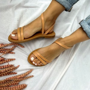 May include: Tan leather sandals with two straps across the foot and an ankle strap. The sandals are on a white background.