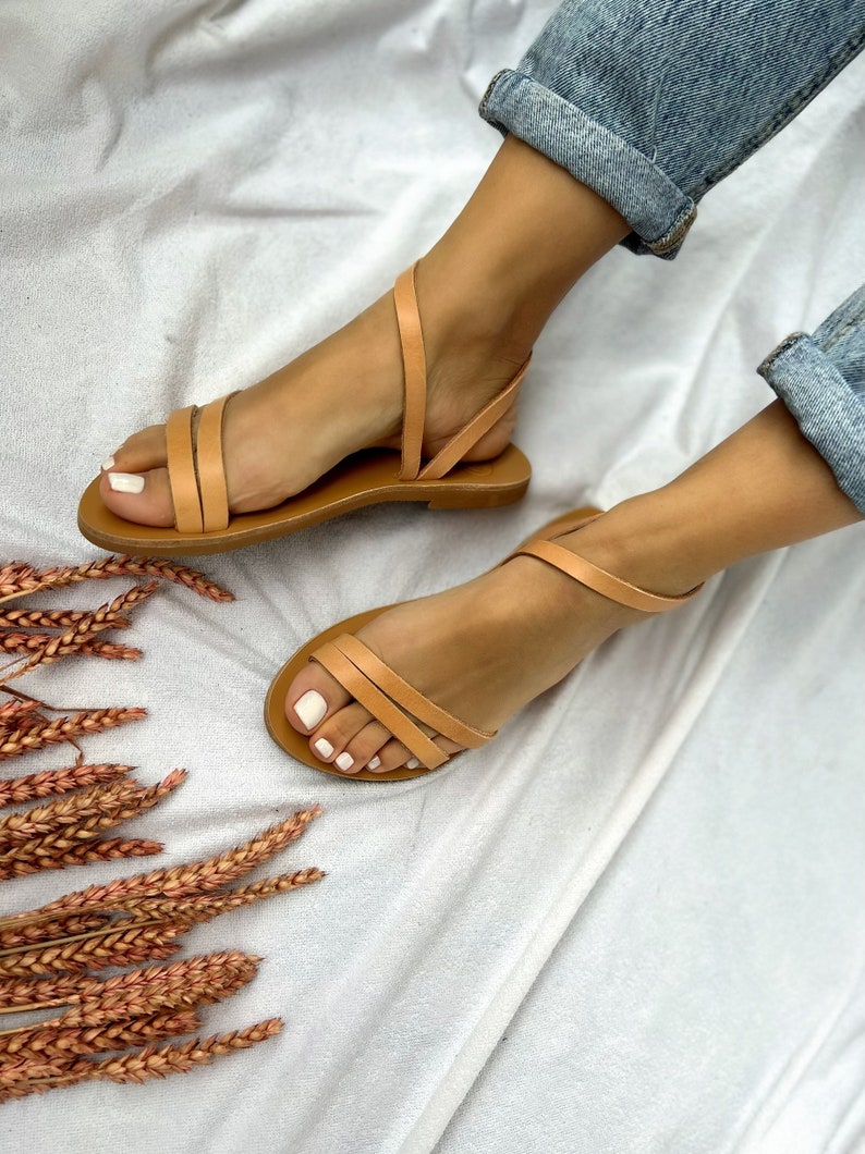 May include: Tan leather sandals with two straps across the foot and an ankle strap. The sandals are on a white background.
