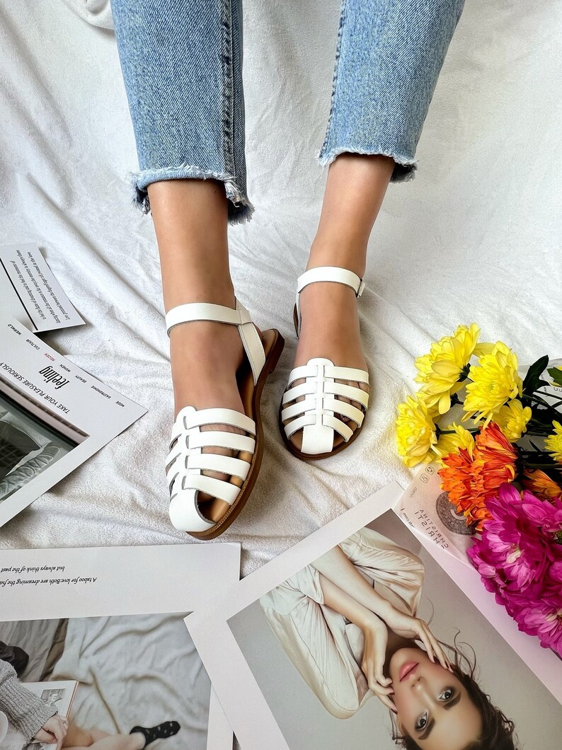 May include: White leather sandals with a woven strap design. The sandals have a buckle closure and a flat sole.