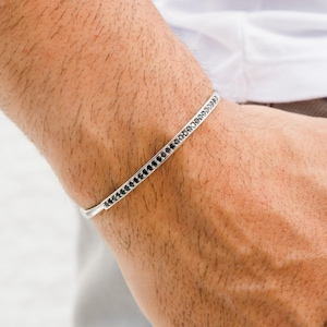 May include: A silver bangle bracelet with a row of black stones around the edge.
