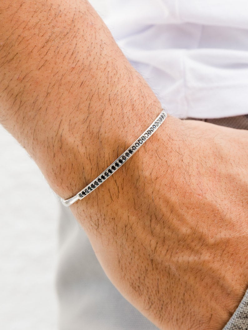 May include: A silver bangle bracelet with a row of black stones around the edge.