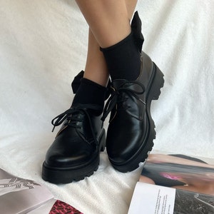 May include: Black leather lace-up platform shoes with chunky soles. The shoes have a bow detail on the back of the ankle.