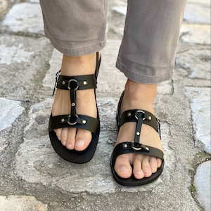May include: Black leather sandals with multiple straps and silver buckles. The sandals have a closed toe and a flat sole.