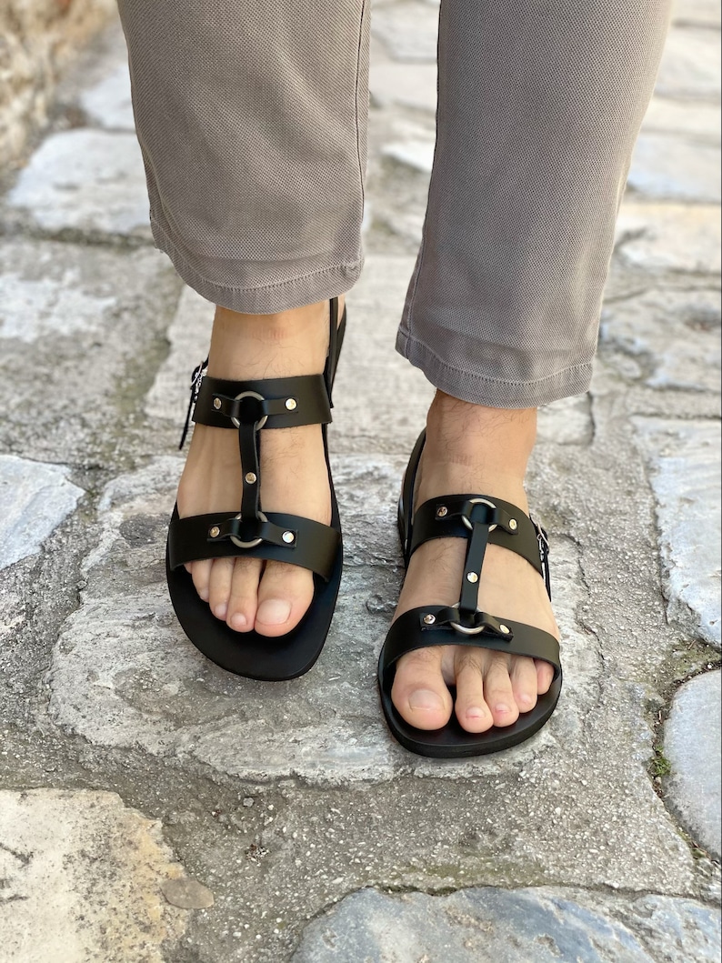 May include: Black leather sandals with multiple straps and silver buckles. The sandals have a closed toe and a flat sole.