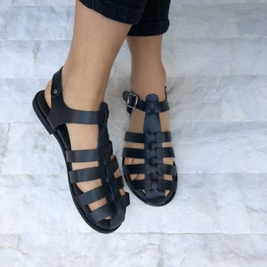 Op de afbeelding: Zwarte leren gladiatorsandalen met een kooiconstructie en gespsluitingen.