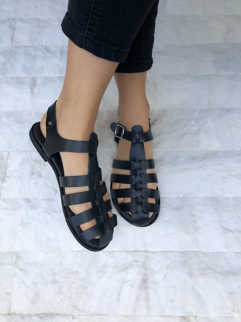 Op de afbeelding: Zwarte leren gladiatorsandalen met een kooiconstructie en gespsluitingen.