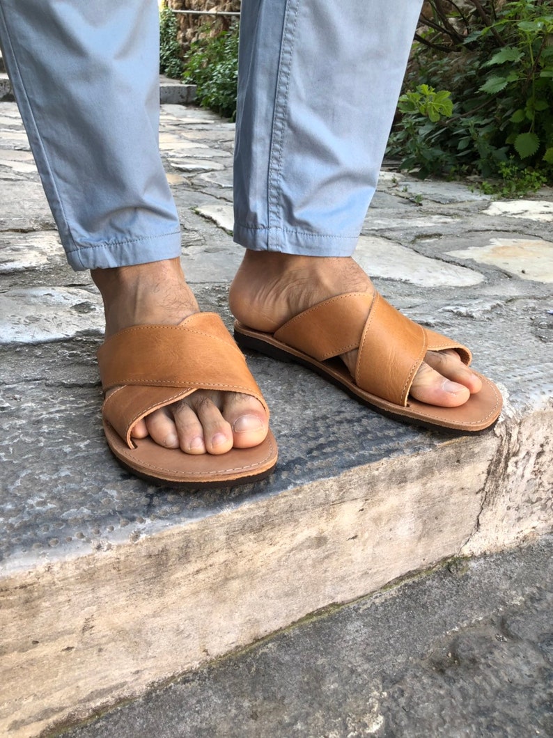 May include: A pair of brown leather sandals with a criss-cross strap design. The sandals are worn on a person's feet, with the toes visible.