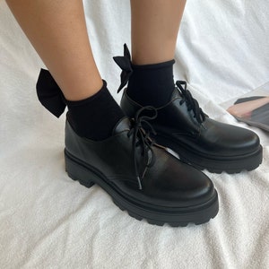 May include: Black leather lace-up shoes with chunky soles and black bow socks.