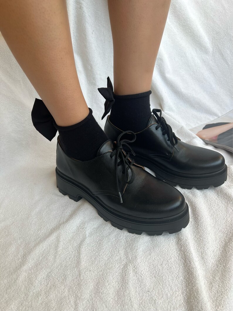 May include: Black leather lace-up shoes with chunky soles and black bow socks.