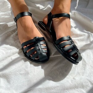 May include: A pair of black caged sandals with adjustable ankle straps. The sandals have a flat sole and are made of a rubber-like material.