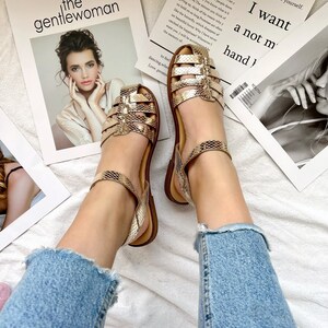 May include: A pair of gold sandals with a snake skin pattern. The sandals have a strap around the ankle and a buckle closure. The sandals are on a white surface with a magazine in the background. The magazine has the text "the gentlewoman" and "GIVE ME sometimes the same thing we can go to the comfort of others, but failed to convince yourself. Nobody can go back and start a new beginning, but anyone can start today and make a new ending. Don't let your goals by what other people deem important. Only you know what is best for you. The minute you think of giving up, think of the reasons why you held on so long. Promises are like the butterfly, which disappear after their beautiful hover. Why I have never caught the happiness? Whenever I want you I will be accepted by the memory of... I want a not my hand!"
