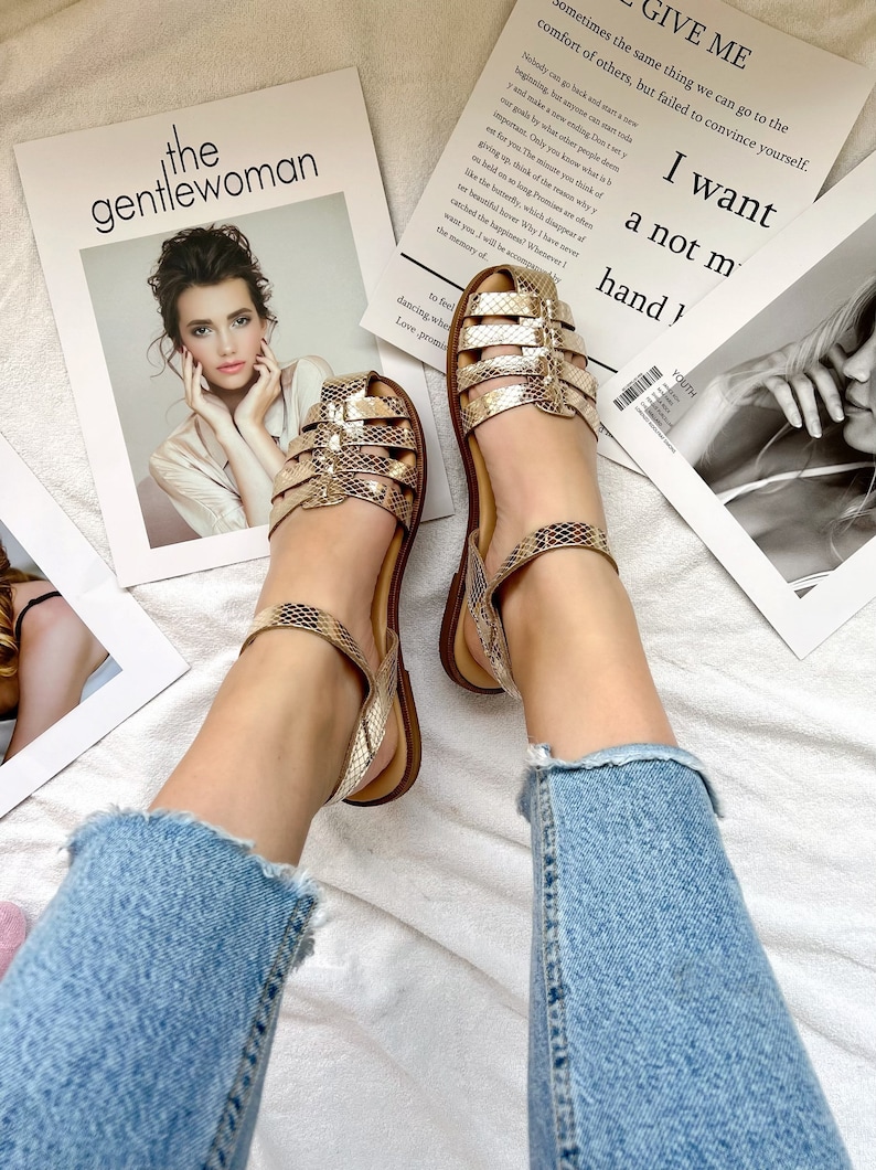 May include: A pair of gold sandals with a snake skin pattern. The sandals have a strap around the ankle and a buckle closure. The sandals are on a white surface with a magazine in the background. The magazine has the text "the gentlewoman" and "GIVE ME sometimes the same thing we can go to the comfort of others, but failed to convince yourself. Nobody can go back and start a new beginning, but anyone can start today and make a new ending. Don't let your goals by what other people deem important. Only you know what is best for you. The minute you think of giving up, think of the reasons why you held on so long. Promises are like the butterfly, which disappear after their beautiful hover. Why I have never caught the happiness? Whenever I want you I will be accepted by the memory of... I want a not my hand!"