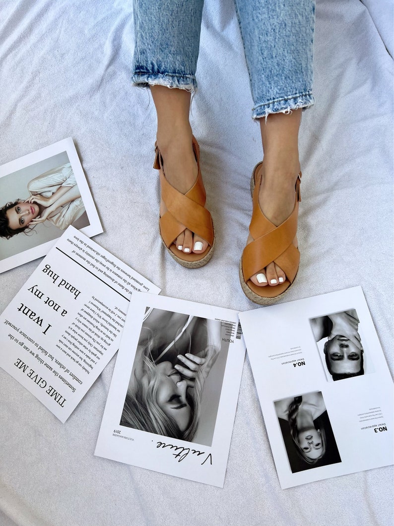 May include: Tan leather sandals with a woven platform sole. The sandals have a criss-cross strap design and a buckle closure. The image also shows pages from a magazine with black and white photos and the text "Vulture."