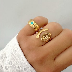 Könnte beinhalten: Zwei goldene Ringe mit türkisfarbenen Steinen. Ein Ring hat ein Augenmotiv und der andere ein Blumenmuster.