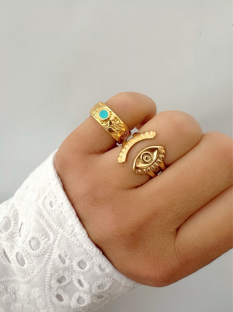 May include: Two gold rings with turquoise stones. One ring features an eye design and the other has a floral pattern.