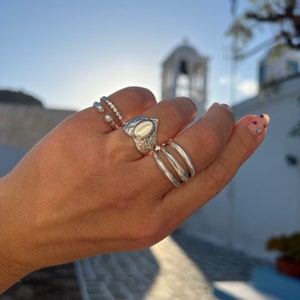 Può includere: Una mano con tre anelli d'argento. L'anello sull'indice ha una grande pietra ovale. Gli altri due anelli sono sottili e delicati.