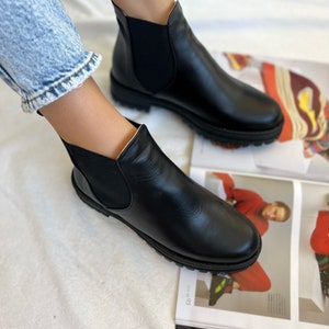 Pu&ograve; includere: Stivali Chelsea in pelle nera con pannelli laterali elasticizzati e punta arrotondata. Gli stivali hanno una suola spessa nera. Mostrati con jeans blu. Stile classico.