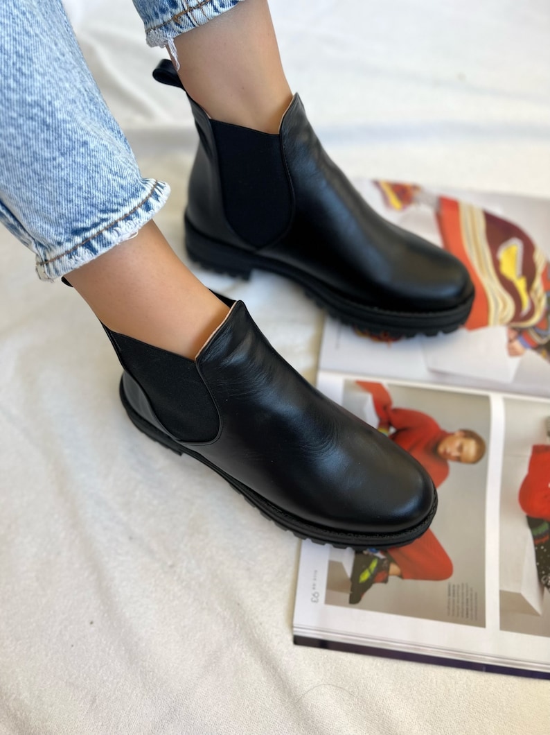 Pu&ograve; includere: Stivali Chelsea in pelle nera con pannelli laterali elasticizzati e punta arrotondata. Gli stivali hanno una suola spessa nera. Mostrati con jeans blu. Stile classico.