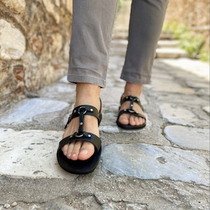 Puede incluir: Sandalias de cuero negro con hebillas y correas. Las sandalias tienen una suela plana y se llevan en los pies.