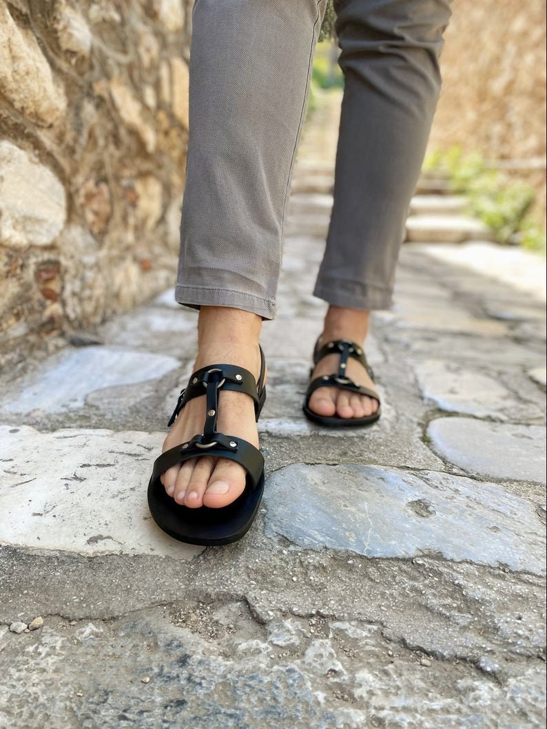 Puede incluir: Sandalias de cuero negro con hebillas y correas. Las sandalias tienen una suela plana y se llevan en los pies.