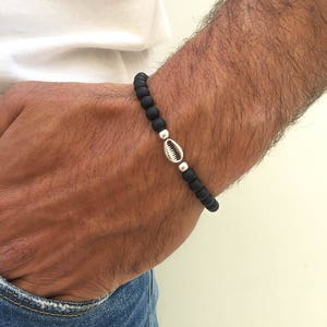 Puede incluir: Un brazalete de cuentas negras con un dije de concha de mar plateado.
