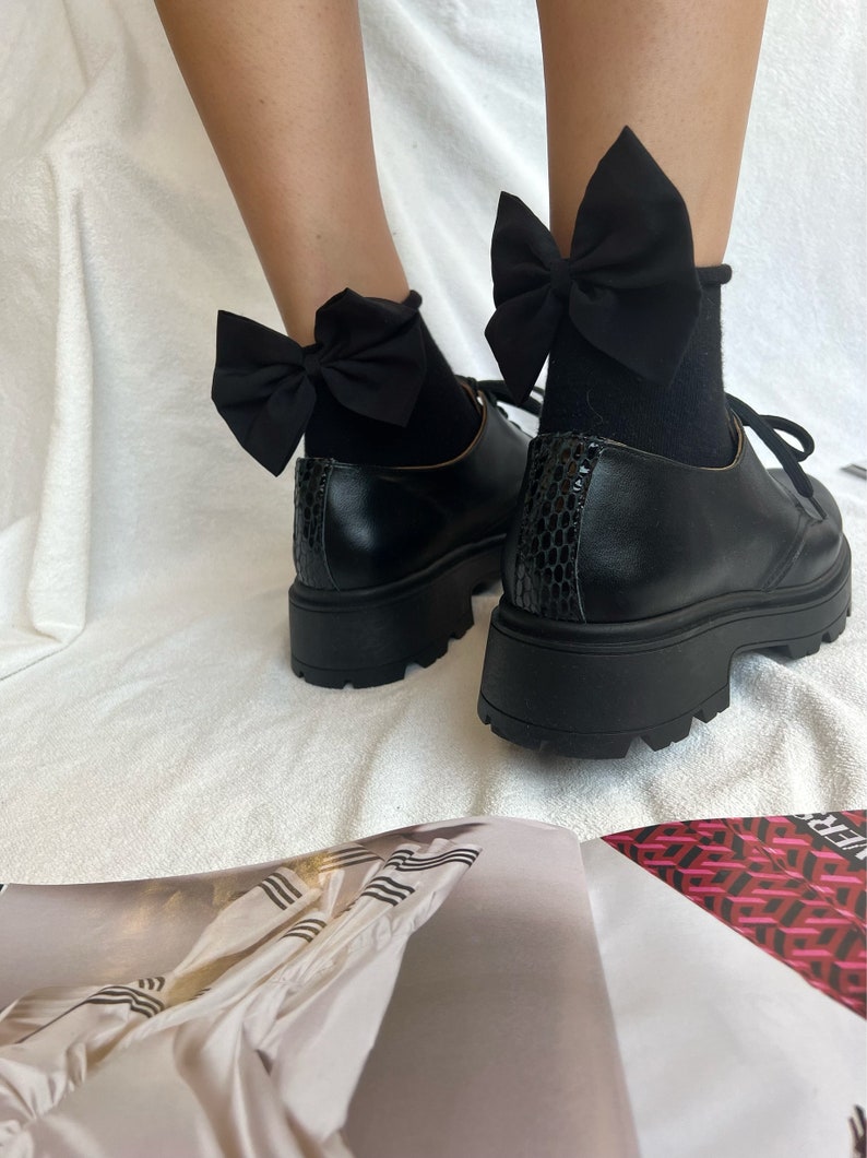 May include: Black platform shoes with black bow socks. The shoes have a chunky heel and a rounded toe. The socks have a large black bow on the top.