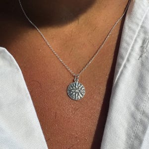Puede incluir: Un collar de cadena de plata con un colgante circular con un diseño de estrella.