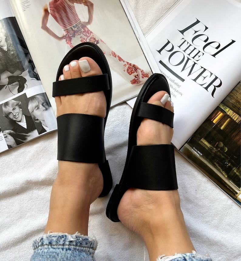 May include: A pair of black leather sandals with two straps across the foot. The sandals have a simple design and are perfect for summer.