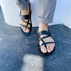 May include: A pair of black leather sandals with multiple straps crossing over the foot. The sandals have a buckle closure on the ankle strap.
