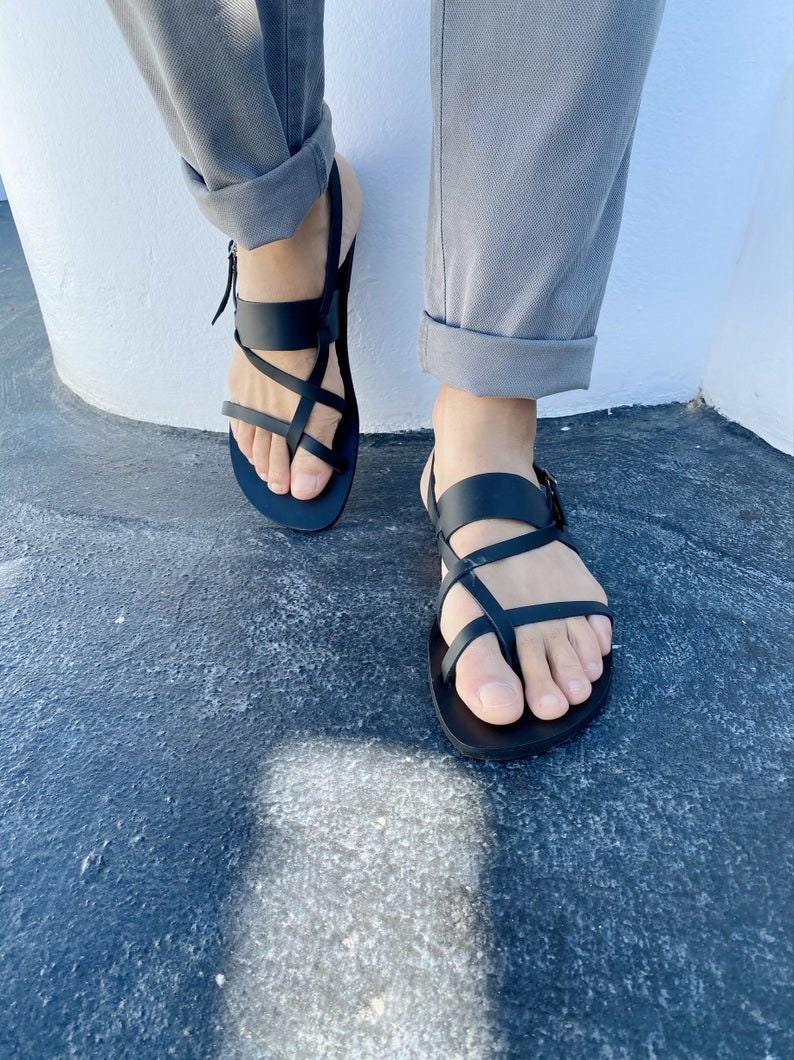 May include: A pair of black leather sandals with multiple straps crossing over the foot. The sandals have a buckle closure on the ankle strap.
