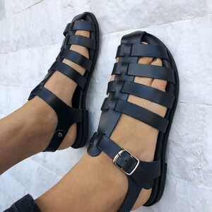 May include: Black leather sandals with a woven strap design and a buckle closure. The sandals have a flat sole and are made of high-quality leather.