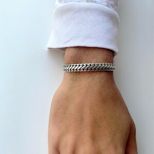 May include: A silver chain bracelet with a textured design. The bracelet is worn on a person's wrist.