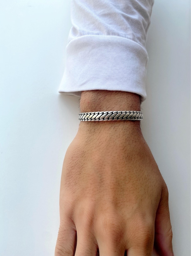 May include: A silver chain bracelet with a textured design. The bracelet is worn on a person's wrist.