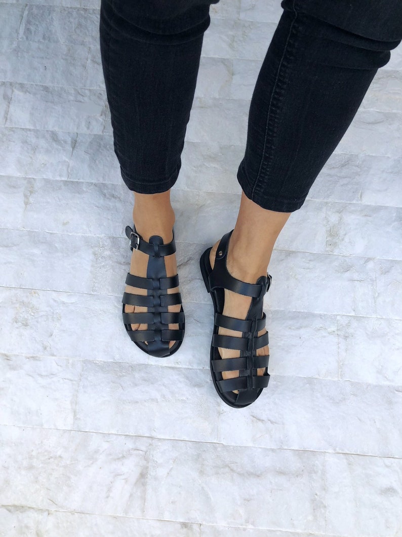 Op de afbeelding: Zwarte leren gladiatorsandalen met een geweven band ontwerp. De sandalen hebben een gespsluiting en een platte zool.