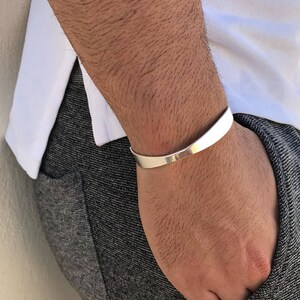 May include: A silver cuff bracelet with a curved design. The bracelet is worn on a person's wrist.