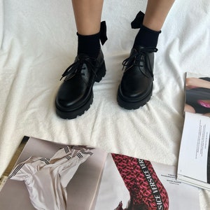 May include: Black leather lace-up shoes with a chunky sole and a black bow on each shoe.