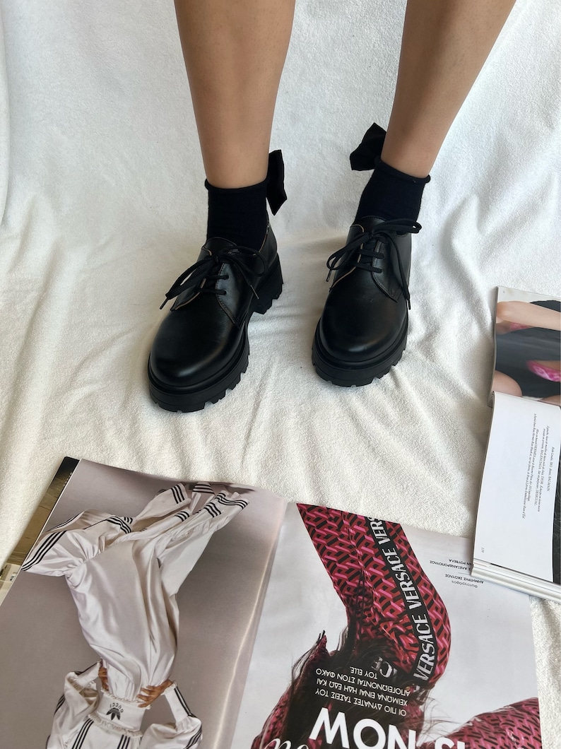 May include: Black leather lace-up shoes with a chunky sole and a black bow on each shoe.