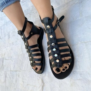 Puede incluir: Sandalias gladiadoras de cuero negro con tachuelas plateadas y cierres de hebilla. Las sandalias tienen una suela plana y est&aacute;n hechas de m&uacute;ltiples correas.