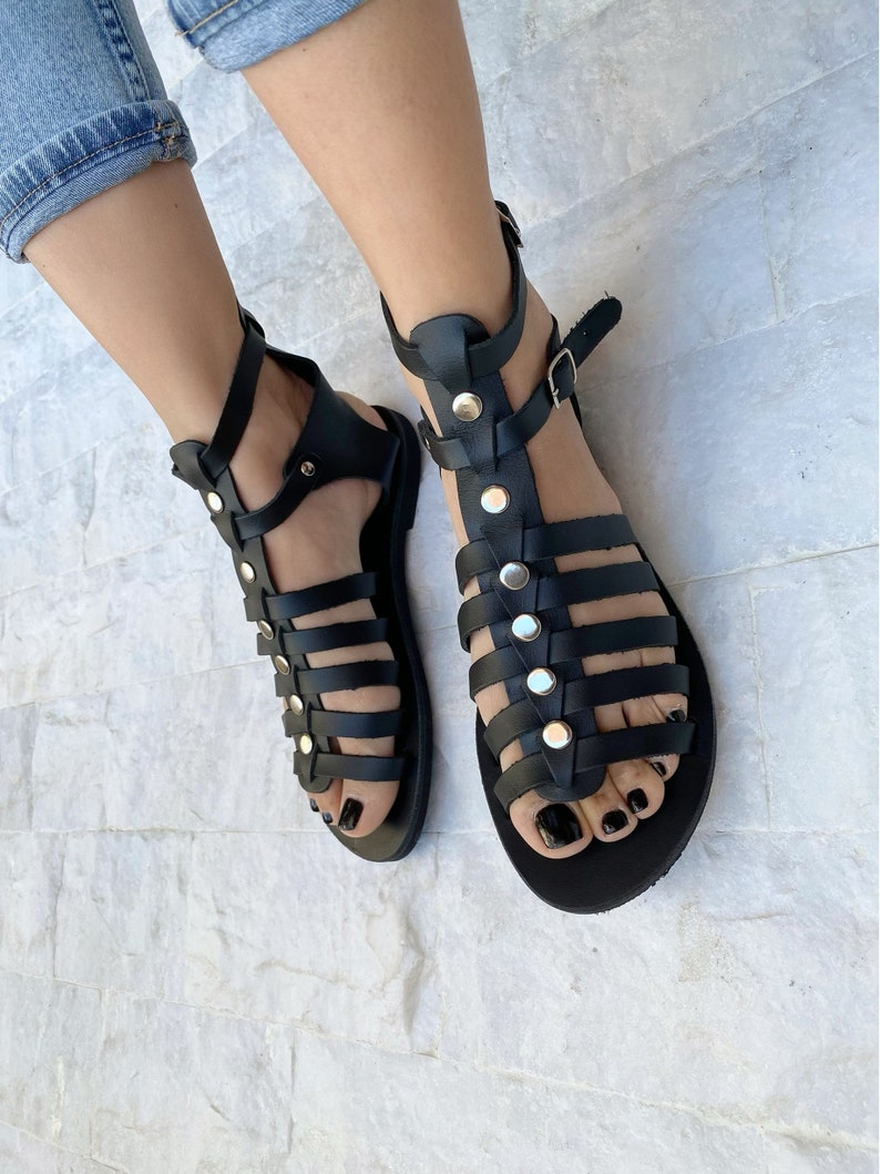 Puede incluir: Sandalias gladiadoras de cuero negro con tachuelas plateadas y cierres de hebilla. Las sandalias tienen una suela plana y est&aacute;n hechas de m&uacute;ltiples correas.