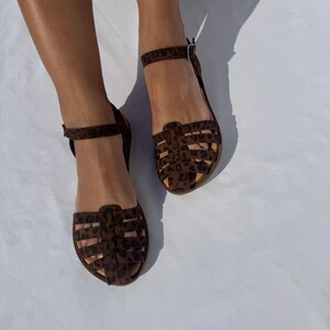 May include: A pair of brown sandals with a leopard print design. The sandals have a caged design and ankle straps.