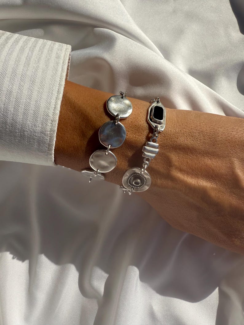 May include: Silver dangle earrings with geometric shapes. One earring features a black rectangular stone. The other earring has three circular discs. The earrings are displayed against a white background.