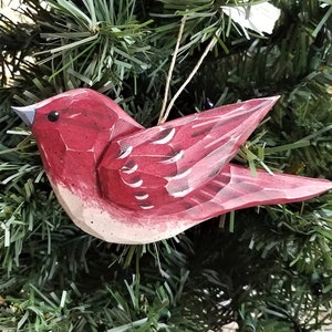 Puede incluir: Un adorno de pájaro de madera pintado a mano en tonos rojos y blancos, con un acabado rústico. El pájaro está colgado de una cuerda y es una decoración festiva para un árbol de Navidad.